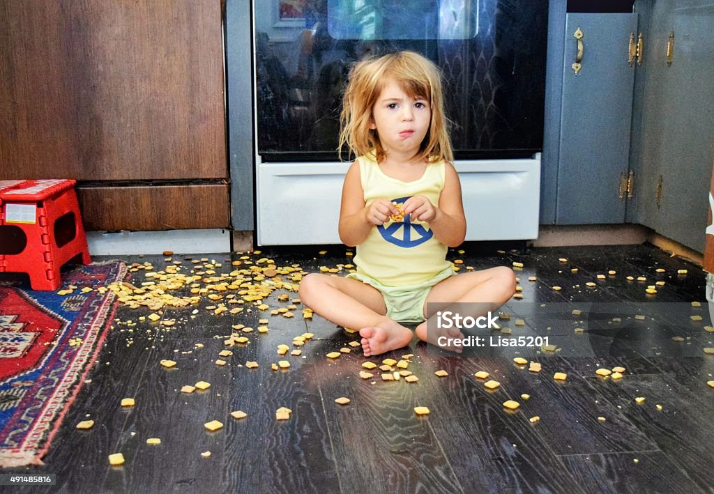 What!? I got my own snack Toddler spills a snack all over the floor, but seems content to eat it anyways Child Stock Photo