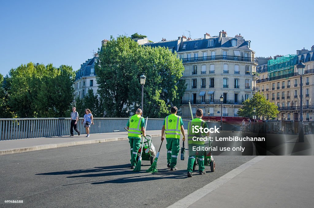 Sanitation workers with garbage carts Paris, France - August 22, 2015: Three sanitation workers cross the St. Louis Bridge to the St. Louis Island with their carts on a sunny, summer day to keep the streets of this popular tourist destination clean.  Sanitation Worker Stock Photo