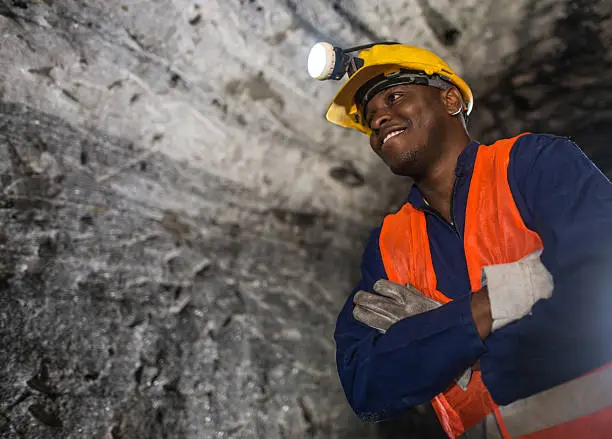 African American miner working at the mine and wearing a helmet with the light on in a dark tunnel