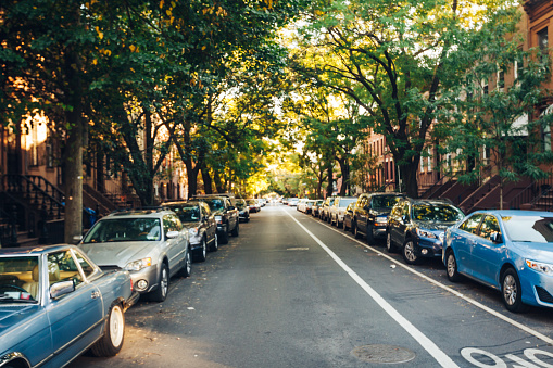 A one-way street in Brooklyn, NY with cars parked on either side