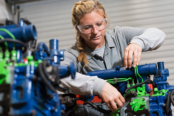 Young woman training to be auto mechanic A young woman in vocational school learning the auto mechanic trade.  She is working on a diesel engine that has been color-coded for educational use. diesel fuel stock pictures, royalty-free photos & images