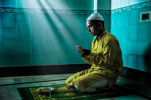 Young Muslim man praying, with folded hands Young Muslim man praying, with folded hands. He is in traditional Indian Attire and sports a skull cap on his head. Sunbeam falling on him. yarmulke photos stock pictures, royalty-free photos & images