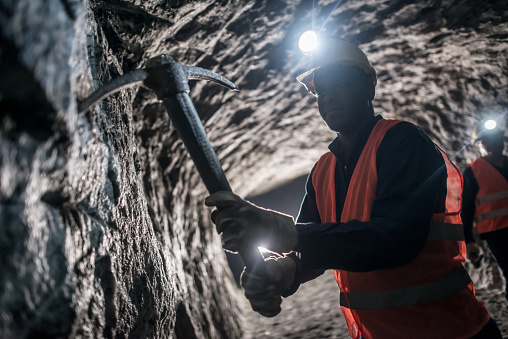 Miner using a pick tool at the mine and working in a dark tunnel