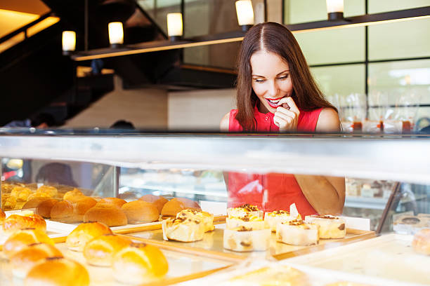 woman choosing bakery items in a shop Female standing in confectionery and trying to chose a cake (looking at left side) display cabinet photos stock pictures, royalty-free photos & images