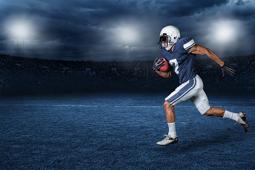 An american football player running with the football during live action of a football game in a large professional stadium. 