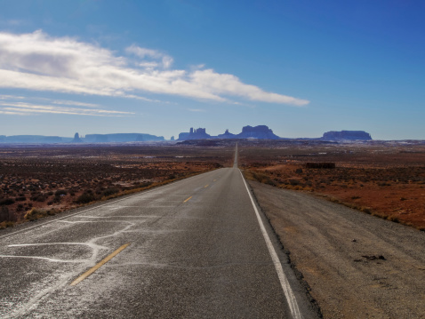 A highway in the American Southwest points to a distant horizon while a dramatic blue sky full of clouds frames the landscape.