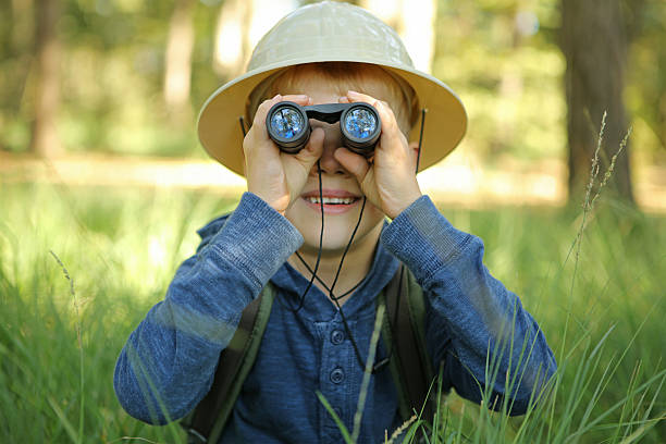 istock Boy in Pith Helmet Hiding in Grass Looking Through Binoculars 491546354