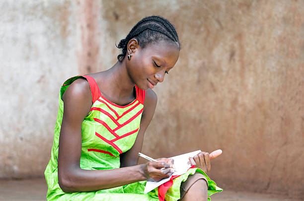 istock Beautiful African Schoolgirl Writing Notes on Exercise Book Education Symbol 491562726