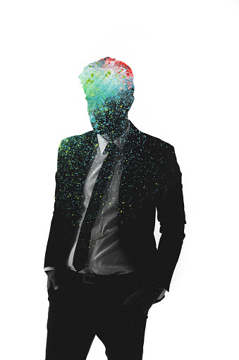 A man standing in a suit in monochrome, isolated against a white background with his face obscured by colours splattered within his form in a graphic representation of creativity