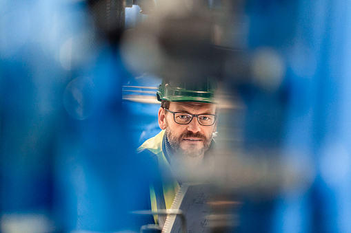 Portrait of confident mature worker at factory. Male professional is wearing eyeglasses. Focus is on manufacturing expert.