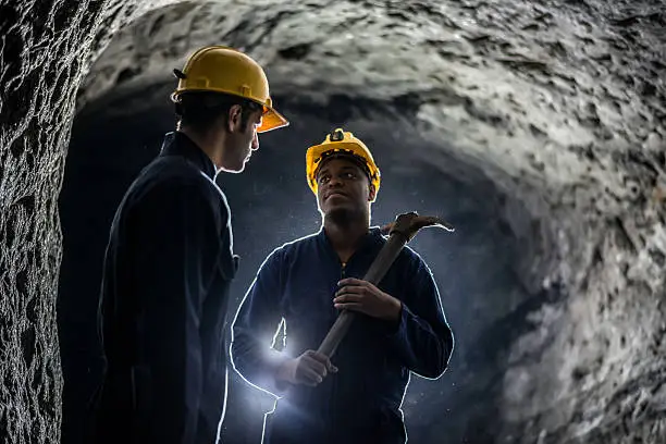 Miners working at a mine wearing helmets and holding tools - mining concepts