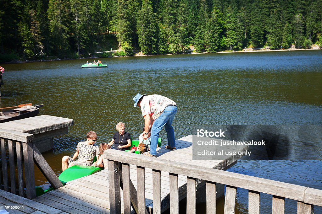 Tourists in recreational boat on lake Mummelsee Seebach, Germany - August 31, 2015: Tourists are sitting in recreational boat on lake Mummelsee in Black Forest. A mature man is helping family to unlock boat. In background more people are in boats on lake. 2015 Stock Photo