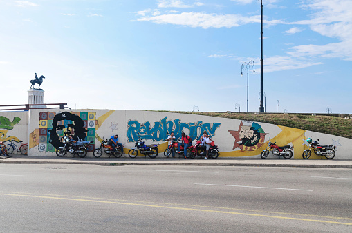 Havana, Cuba - August 10, 2015: Bikers with bikes spend time at the wall with graffitis. Graffitis are represented in various Cuban revolutionaries.