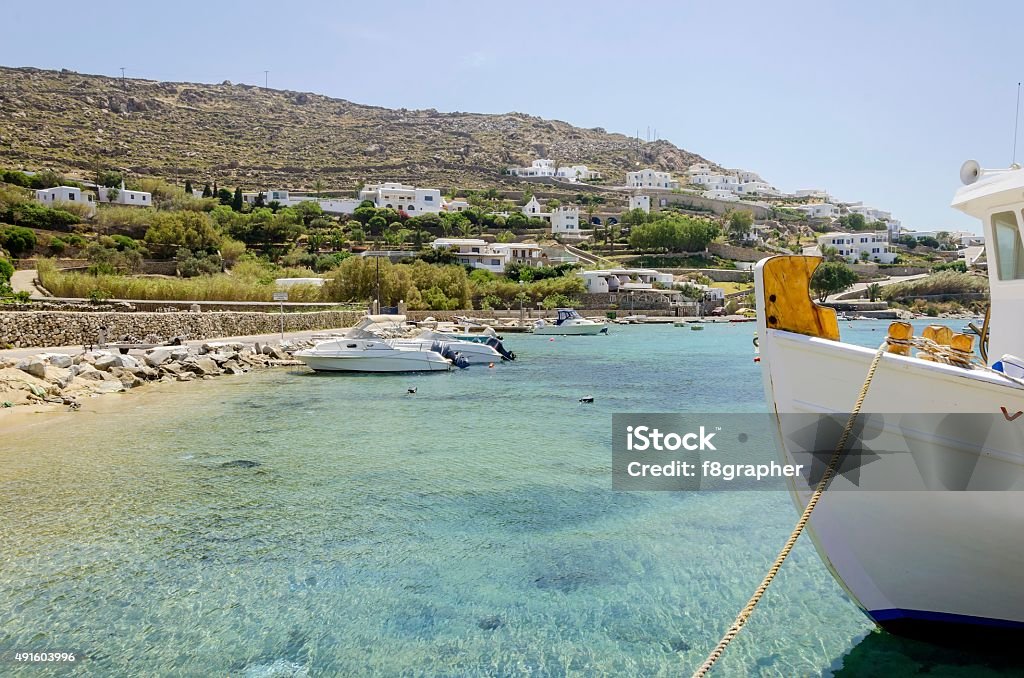 Ornos beach, Mykonos, Greece Fishing boats docked at Ornos beach in Greece. A view of the crystal clear blue sea at the greek island Mykonos, and whitewashed houses on the hill slope. A typical, idyllic summer holiday beach scene. Mykonos Stock Photo