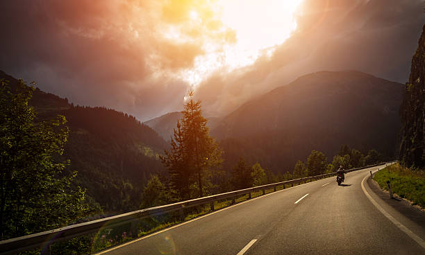 Motorcyclist in action, bright red sunset light, overcast weather, active lifestyle, traveling along Alpine mountains, extreme adventure concept