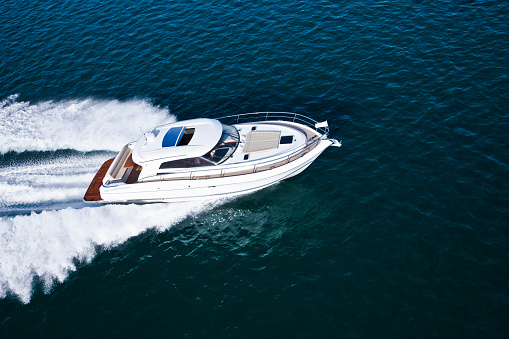 Aerial shot of a beautiful white motor boat with brown details sailing across the sea