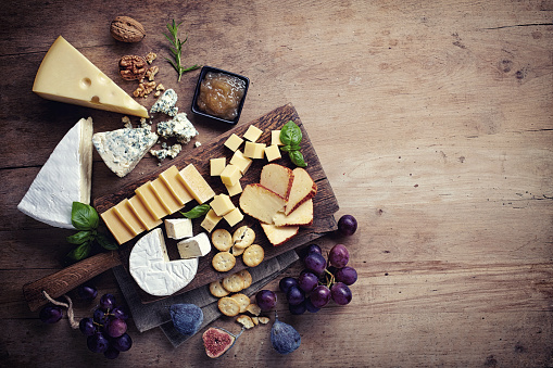 Cheese plate served with grapes, jam, figs, crackers and nuts on a wooden background