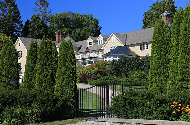 Luxury New England House, Kennebunkport, Maine, USA. Kennebunkport, ME, USA - September 16, 2015: Luxury New England House  with grey shingle exterior, Kennebunkport, Maine, USA. Landscaped front yard, driveway, fence, green grass, bushes, trees, and vivid clear blue sky are in the image. Canon EOS 6D (full frame sensor) and Canon EF 24-105mm f/4 L IS lens. Polarizing filter. driveway colonial style house residential structure stock pictures, royalty-free photos & images