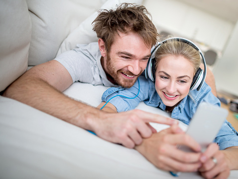 Couple relaxing at home listening to music on a smart phone with headphones