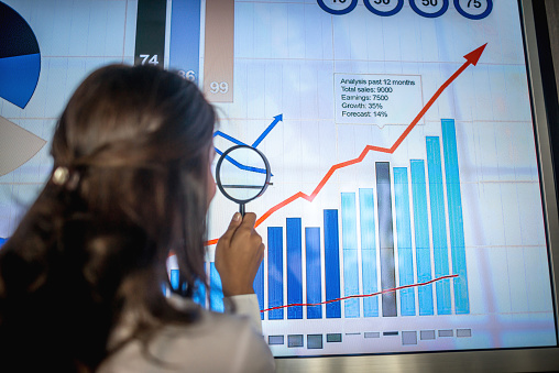 Business woman doing marketing research and holding a magnifying glass while looking at statistic graphs