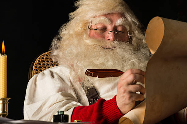 istock Santa Claus sitting at home and writing on paper roll 491635546