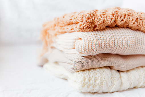 Pile of beige woolen clothes on a white background. Warm knitted sweaters and scarfs are folded in one heap