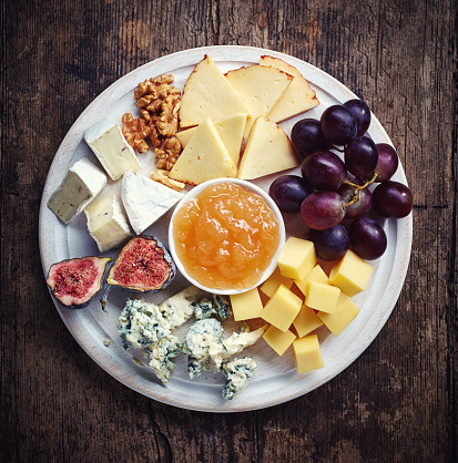 Cheese plate served with grapes, jam, figs and nuts on a wooden background
