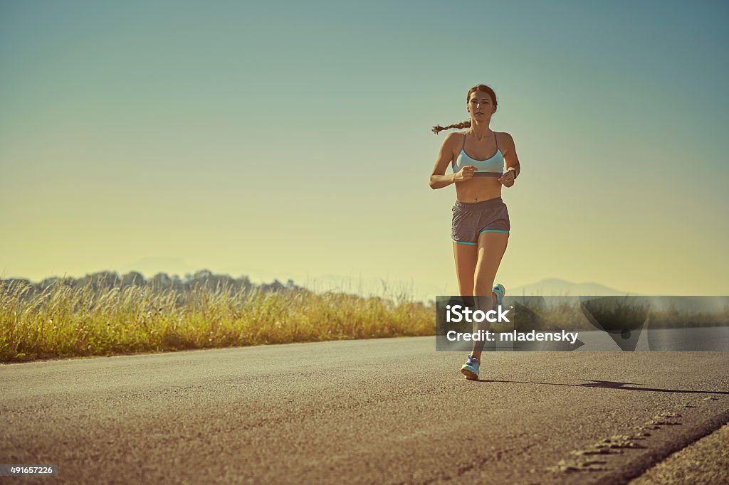 Sporty woman running Active sporty woman in summer sportswear running, sprinting on a road at sunrise or sunset. Health care, body care, healthy lifestyle, willingness concept. Toned color edit. Women Stock Photo