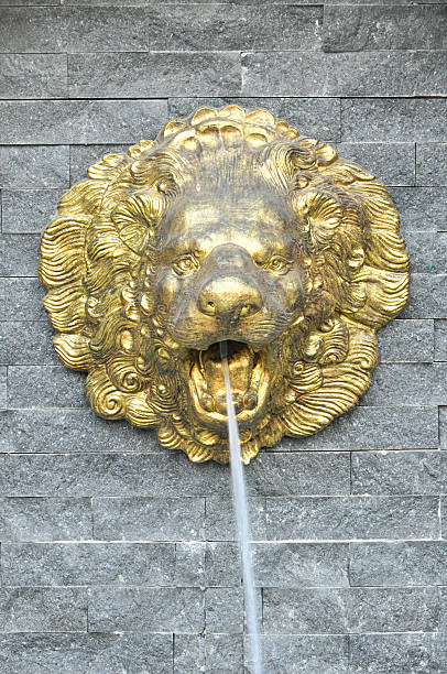 istock Golden lion head sculpture spouting water on stone wall 491665093