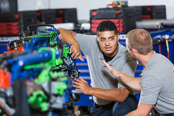 Two multi-racial men in auto mechanic school with engine Two multi-ethnic young men in vocational school, taking a class on reparing diesel engines.  They are working on an engine that has had parts painted different colors for training purposes.  They are wearing safety glasses. multiengine stock pictures, royalty-free photos & images