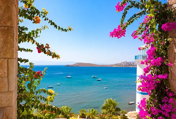 Beautiful flowers can be seen past the Lighthouse at Ortakent in Turkey with blue/green seas stretching to the horizon.