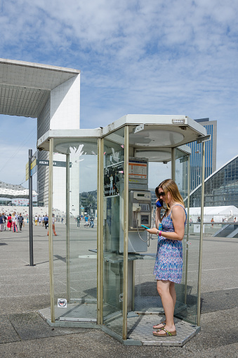 Paris, France - August 11, 2015: Public phones are still available for placing calls at the La Defense complex with the La Grande Arche de la Fraternite in the background.