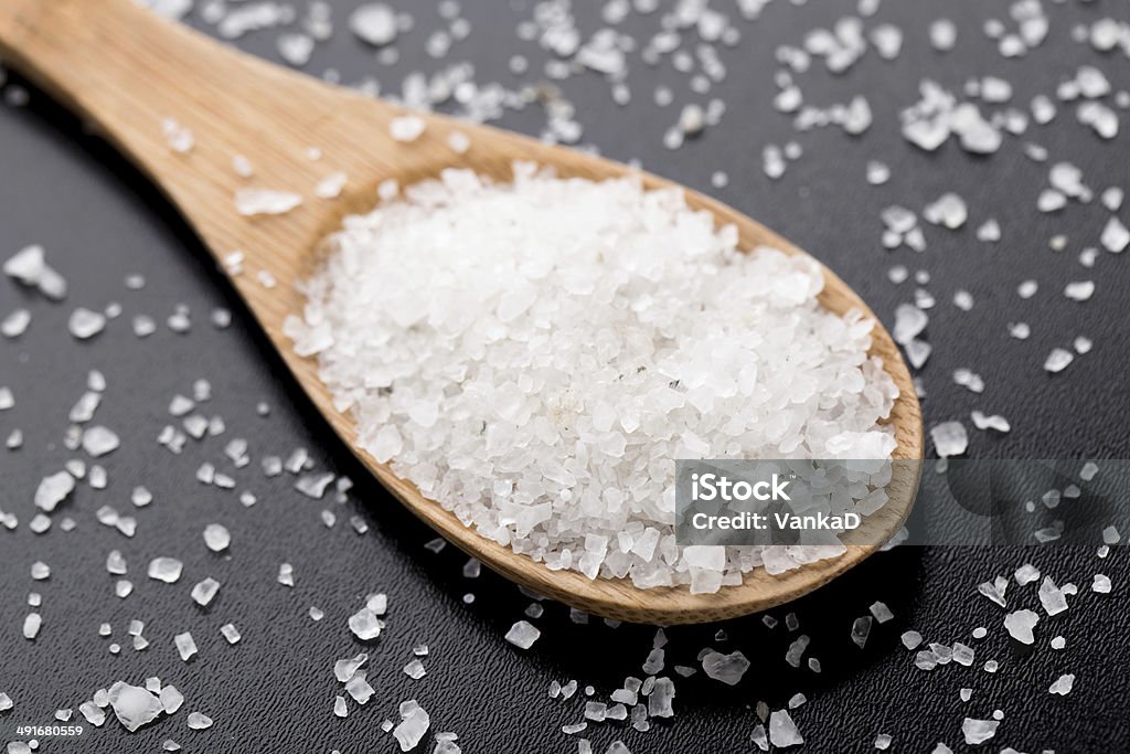 Sea salt in wooden spoon Sea salt in wooden spoon on a black table Backgrounds Stock Photo