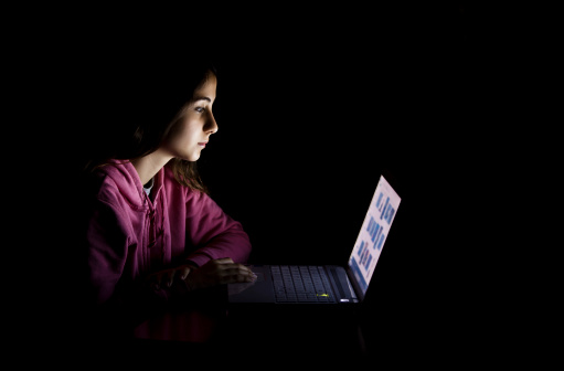 A young woman looking sadly at the monitor of her computer.