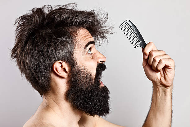 Scared bearded man with messy hair staring at a comb Close-up of a long bearded man with crazy hairstyle and scared expression screaming and staring at a huge comb bushy stock pictures, royalty-free photos & images