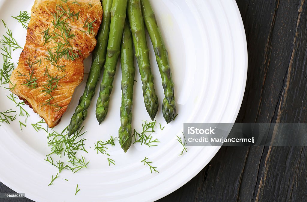 Salmon Fillet With Asparagus on White Plate Salmon fillet with asparagus and dill on white plate dark rough wood Appetizer Stock Photo