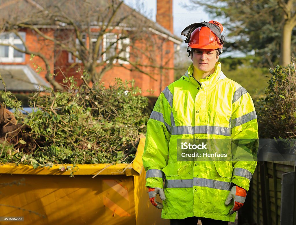 Tree surgeon in front of skip full of tree cuttings Tree surgeon standing in front of skip full of tree cuttings Skipping Stock Photo