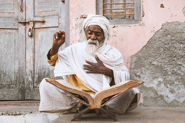 Old indian sadhu reading scriptures. Varanasi, India - November 23, 2014: Old indian sadhu sitting and reading sacred texts near the temple. caste system stock pictures, royalty-free photos & images