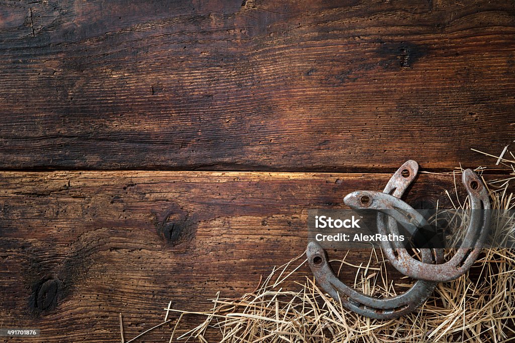 Two old rusty horseshoes with hay Two old rusty horseshoes with hay on vintage wooden board Wild West Stock Photo