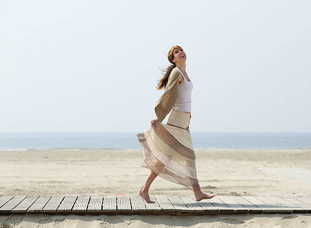 despreocupada mujer madura caminando descalzo en la playa - one person beautiful barefoot beach fotografías e imágenes de stock