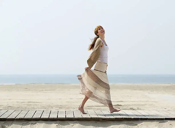 Full length portrait of a carefree mature woman walking barefoot at the beach