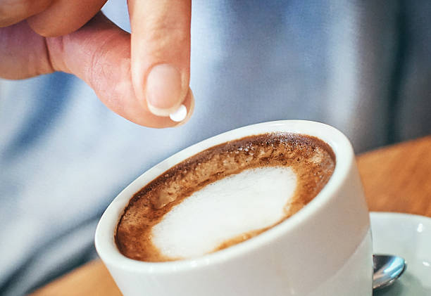 Closeup of unrecognizable woman putting one piece of artificial sweetener into her coffee. These sweeteners are based on aspartame or acesulfam compunds . Tilt shot.