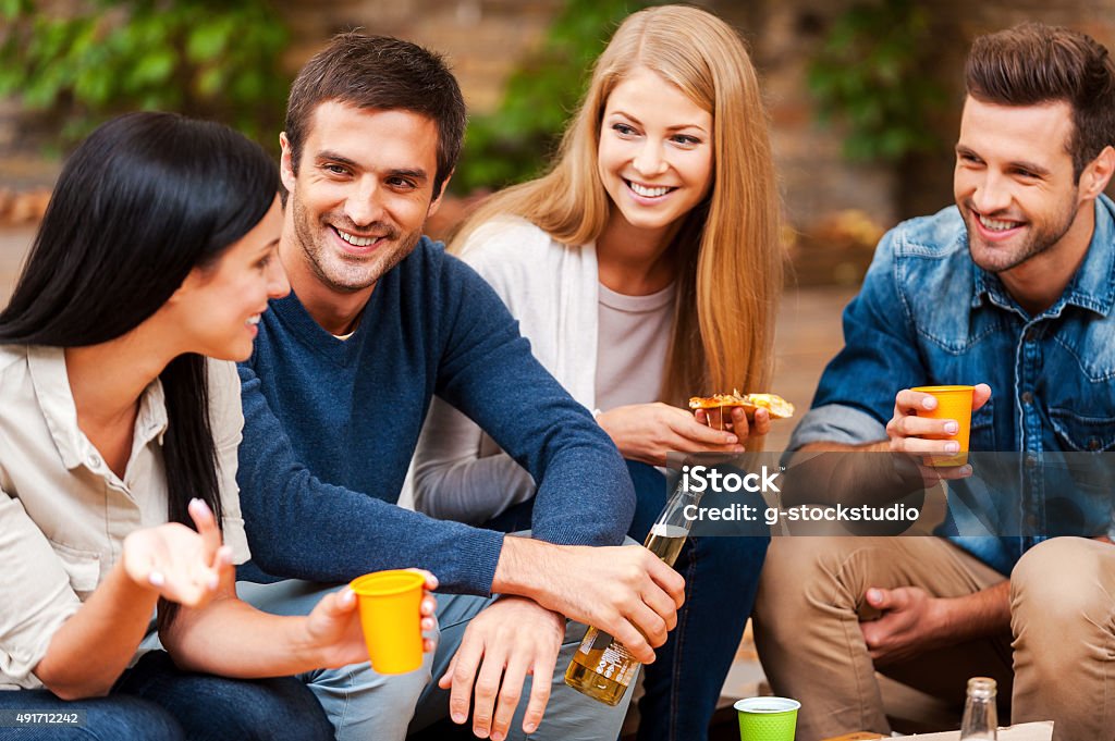 Sharing the latest news. Group of happy young people talking to each other and drinking while sitting outdoors 2015 Stock Photo