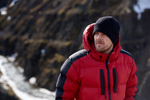 portrait of man in wilderness rugged mountain landscape determined to climb to the summit in red snow gear