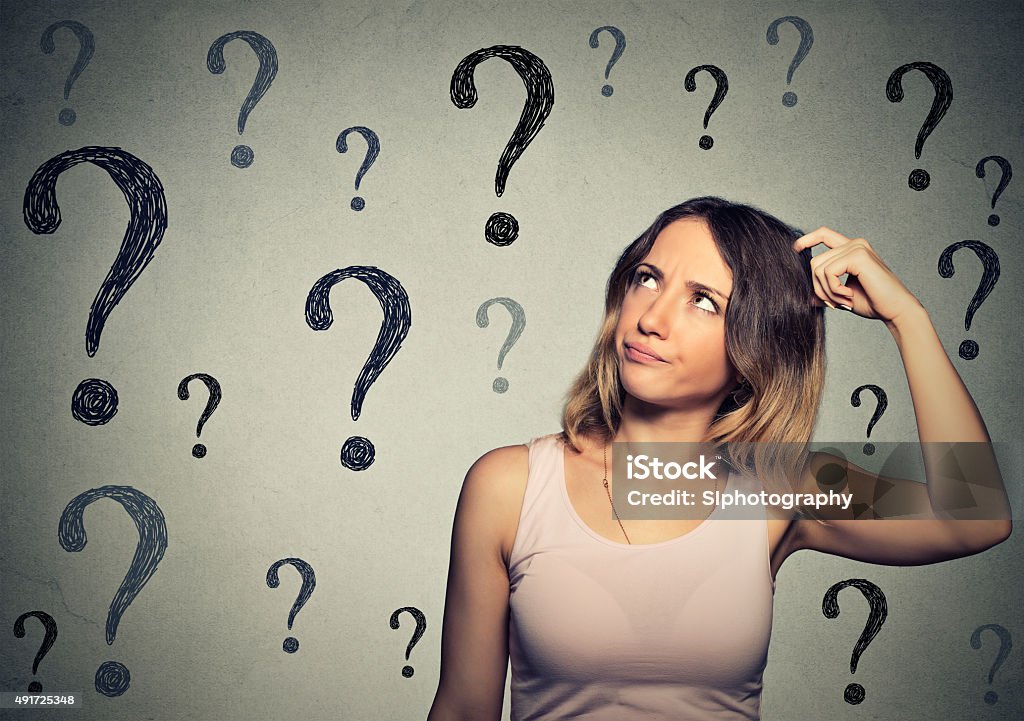 Thinking woman looking up at many question marks Thinking young woman looking up at many question marks isolated on gray wall background Reminder Stock Photo