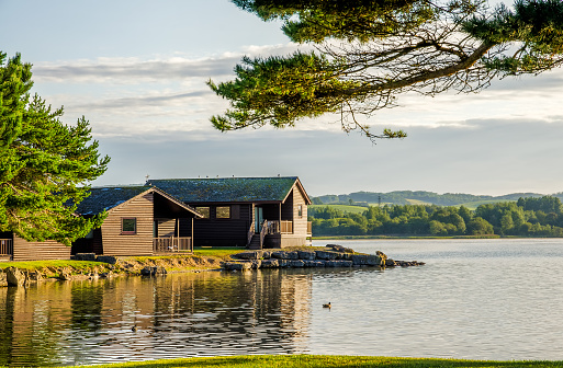 A peaceful scene of wooden holiday lodges bwside a still lake