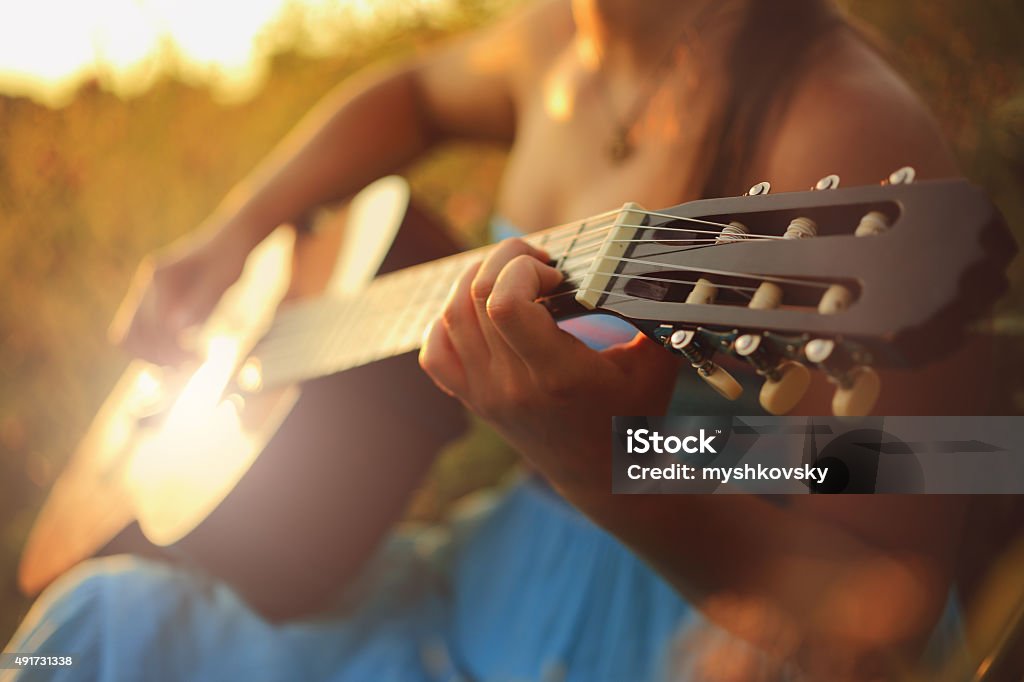 Beautiful woman playing the acoustic guitar in field Beautiful woman in blue dress playing the acoustic guitar in field. Guitar Stock Photo