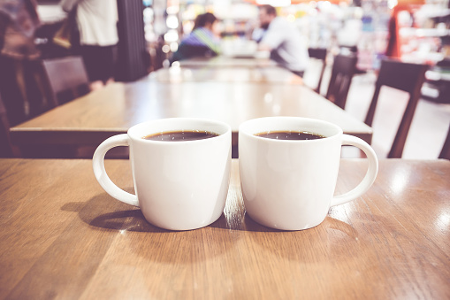 Vintage filter, couple of White coffee cup on wood table with blurred cafe bokeh light background.