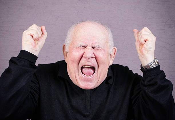 Very emotional old man screams on a gray background.