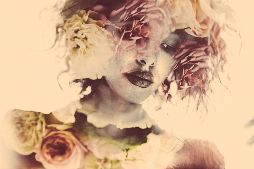 Romantic image of a woman with images of feminine dahlia flowers placed within her form using double exposure effect in soft colours